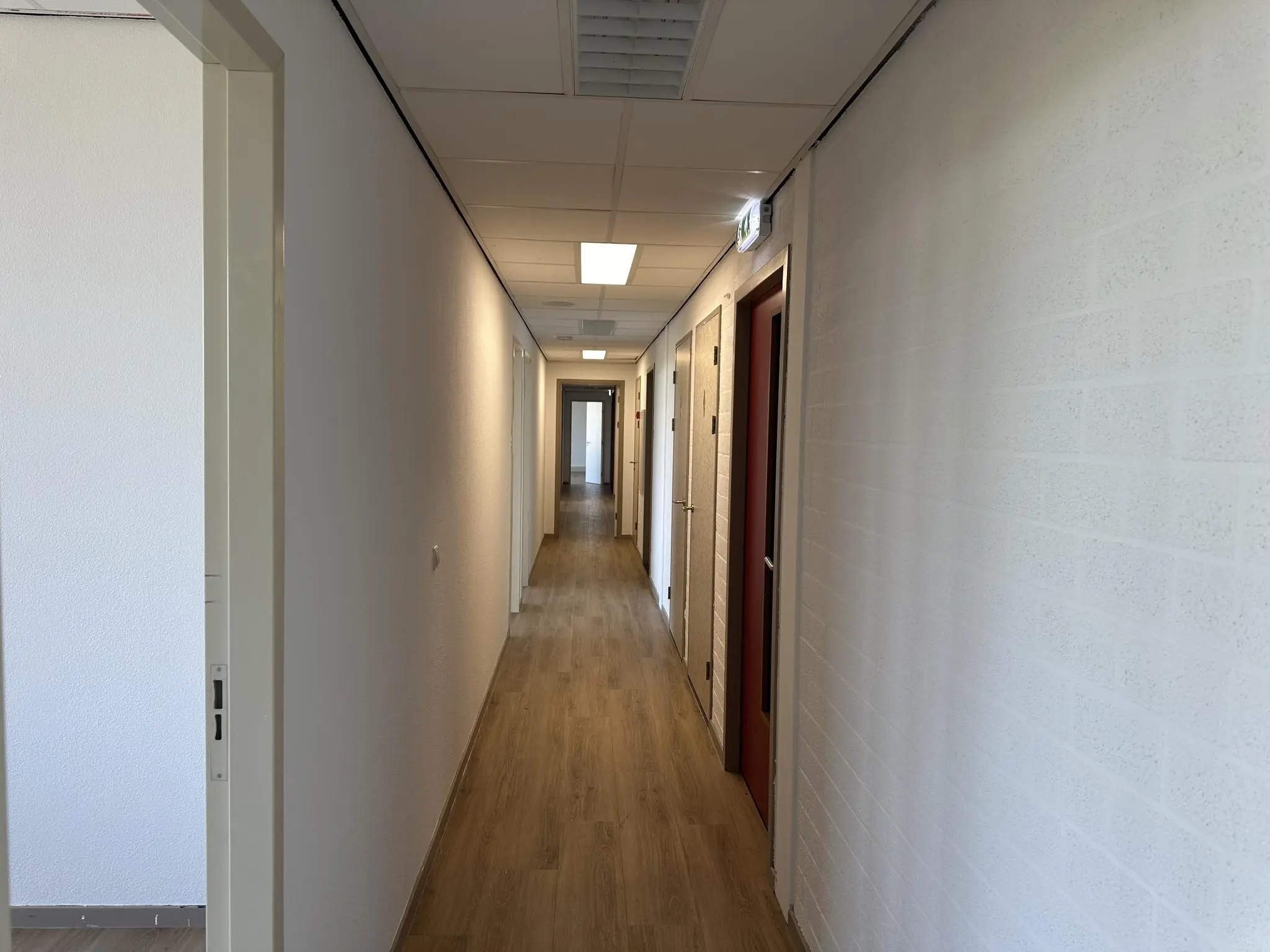 Lange, lichte gang in een kantoorpand aan de Van der Hagenstraat met houten vloer en meerdere deuren.